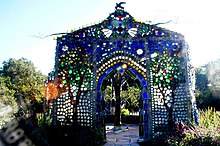 a small house-like structure made of multicolored bottles