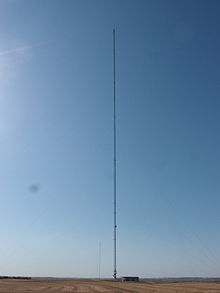 A very tall, guyed broadcast tower in a field