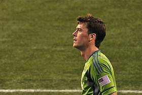 A grown Caucasian man in a light green shirt stares to the camera's left against a green background