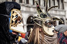 Two people obscuring their faces with festive masks during a Carnival celebration.