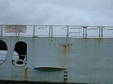 Close-up of a ship's light blue hull with the word «Cardiff» embossed on to it. There is rust drizzling down from the lettering.