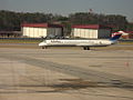 A Delta Air Lines MD-88 taxis past the two United States Air National Guard 117th Air Refueling Wing hangars, a 117th KC-135, and the airport fire station at Birmingham–Shuttlesworth International Airport.