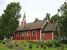 Foto einer roten Holzkirche, davor stehen mehrere Grabsteine