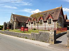 Picture of the Wesley Methodist church in Front Street, Churchill, taken from the opposite side (south) of the road. The church is shown with red painted window ledges and the cemetery surrounded by red railings.