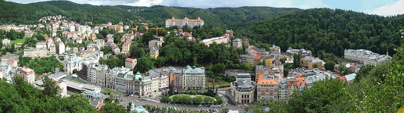 Panoraamvaade Karlovy Varyle. Fotol vasakult paremale: vasakul all 1975. aastal valminud funktsionalistlikus stiilis tumehall Kuumaveekolonnaad, vasakul keskel Maarja-Magdaleena kirik, ülal keskel Hotel Imperial, all keskel (väljakust paremal) ooperiteater, paremas servas Grandhotel Pupp