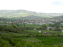 In eine hügelige und begrünte Landschaftlich vor dem Horizont eingebettete Gemeinde und dem bewölkten Himmel am Horizont.