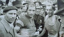 Photographie en noir et blanc de deux cyclistes entourés par une foule.