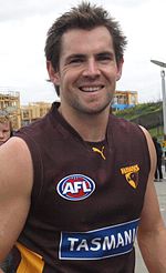 Portrait photograph of man wearing brown and gold guernsey, smiling