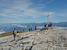 Randonneurs se pressant autour d'une grande croix et profitant d'un large panorama.