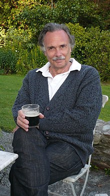 A man with a moustache wearing a white polo and grey sweater