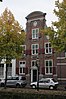 Huis met zware halsgevel met bakstenen pilasters; gebeeldhouwde natuurstenen vleugelstukken, gebeeldhouwde guirlandes en cartouches