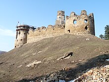 A ruined stone fortress with the remains of a large and a small bastion on the top of a hill