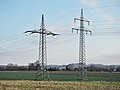 Afspanmast links, steunmast rechts. Verschillen: boogjes (bretels) bij de afspanmast, en richting van de isolatoren. De geleiders zitten bij de afspanmast bijna even hoog als de traverse, en bij de steunmast er onder.