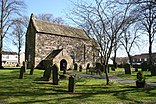 A small plain church building with a stone porch and no tower. It is surrounded by a graveyard and trees without leaves.