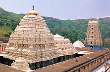 A three-tier yellow coloured pyramid like structure with sculptures and carvings to the left and a five tier tower to the right.