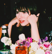 A woman wearing a black T-shirt while resting her elbows on a table.