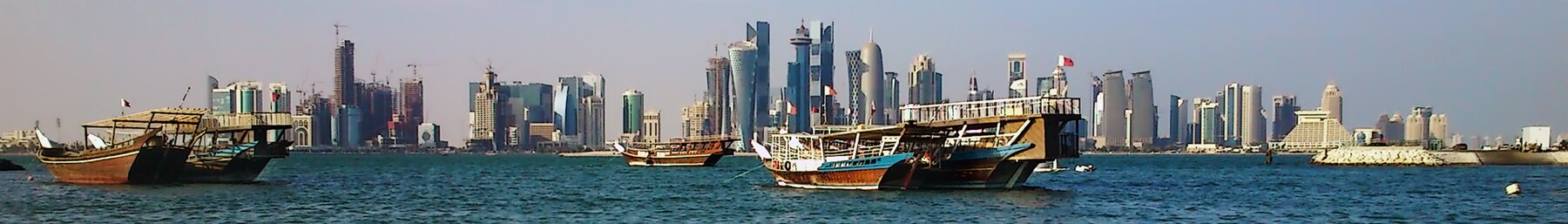 A view of traditional dhow boats in front of the glimmering Doha Corniche