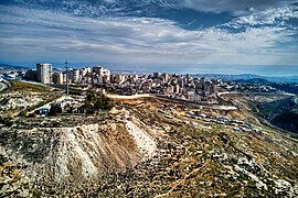 גדר ההפרדה מתפתלת ומקיפה את מחנה הפליטים שועפאט ואת ענאתא. לפני הגדר ניתן לראות מבנים של בדואים ובמרחק את מ��בר יהודה, בקעת הירדן ועבר הירדן.