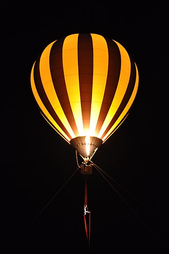 Von einem Heißluftballon hängen Tücher, an denen ein Vertikaltuchakrobat hängt