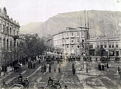 A picture of a city square with people walking about and people riding in carriages.