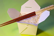 A plain oyster pail, lid opened, without a wire handle, containing plain white rice with a pair of chopsticks laid across the top