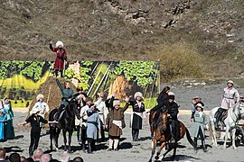 Foule de gens portant des chapeaux traditionnels accompagnant deux cavaliers sur leurs chevaux