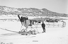 Photo en noir et blanc d'un avion sans ailes sur la neige, un homme s'appuyant sur sa queue.