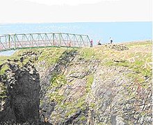 A narrow metal bridge crosses a steep gorge