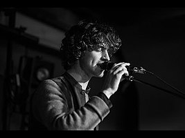 black-and-white image of Cosmo Sheldrake standing onstage, singing into a microphone