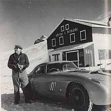 Photo noir et blanc d’un homme à côté d’un coupé, dans un paysage enneigé de montagne.