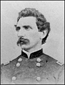 Black and white photo shows a man with wavy hair and a moustache. He wears a dark military uniform.