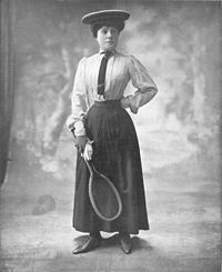 femme en chemisier, jupe longue et corset posant raquette de tennis à la main.