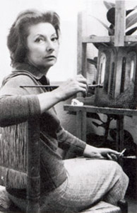 Black and white photo of a middle-aged Remedios Varo sitting at her easel, holding a paintbrush.