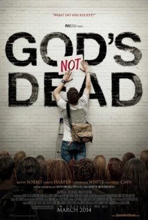 In front of a crowd, a young man on a stepladder puts a piece of paper, with the word "NOT" written on it, in between the words "GOD'S" and "DEAD" which were painted on a wall.