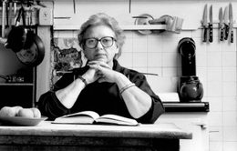 An elderly Grigson seated at a table in a kitchen