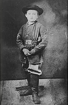 Boy wearing Union uniform, hat, and boots, looks into the camera.