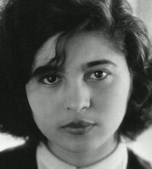 Full-face publicity shot of young, woman with dark, shoulder-length wavy hair, looking directly at the camera.