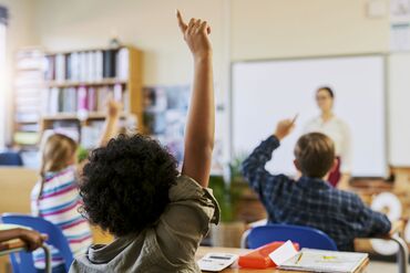 Shot of an unrecognizable group of children sitting in their school classroom and raising their hands to answer a question