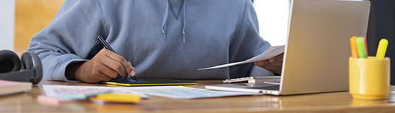 Student working on laptop and writing on paper