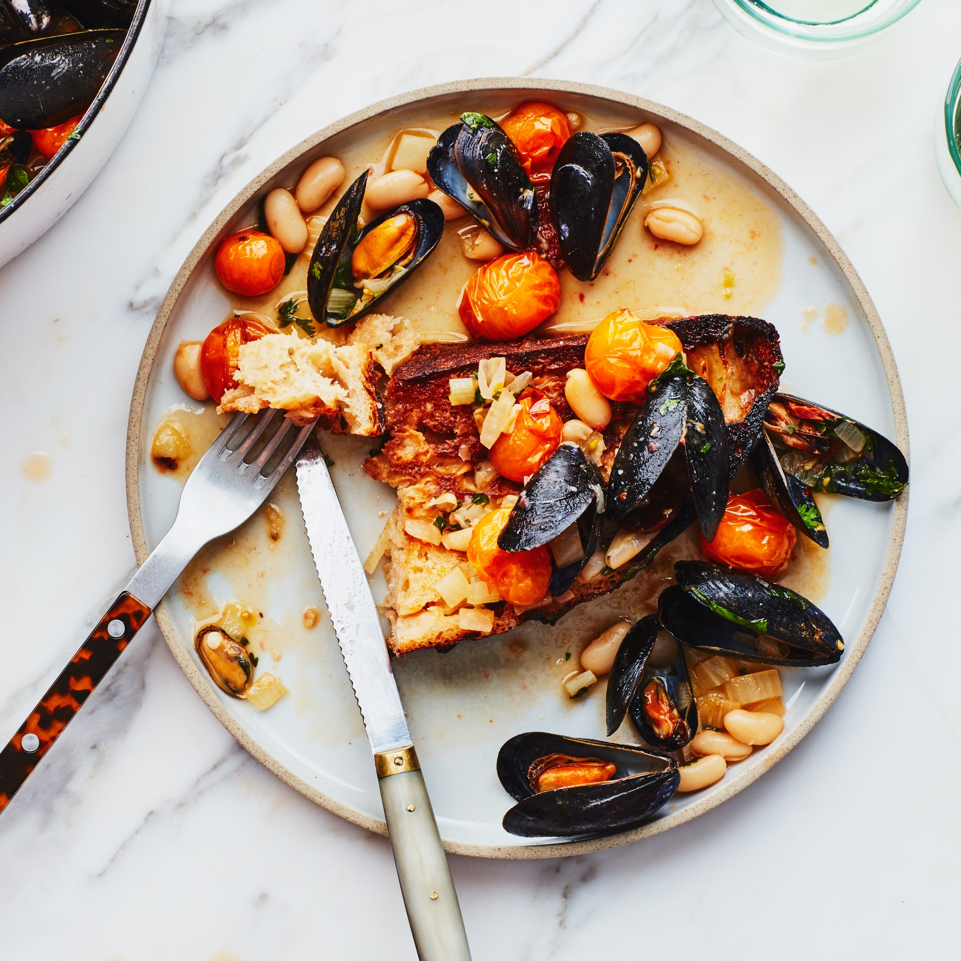 A single serving of mussels on toast with grape tomatoes and white beans.