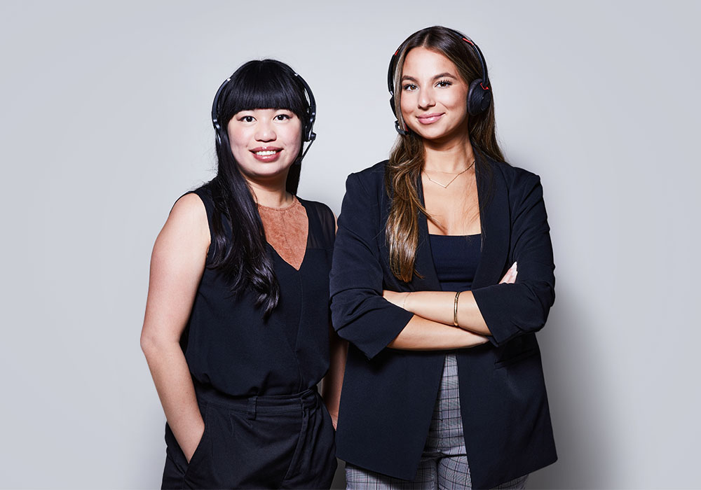 Two Lightspeed customer service agents wearing headsets pose side by side smiling, appearing professional, confident and friendly.