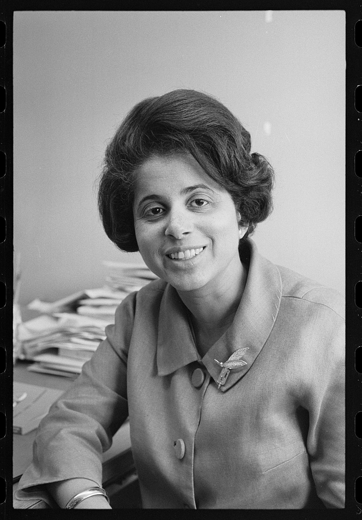 Harris smiling at camera with piles of papers on table in background