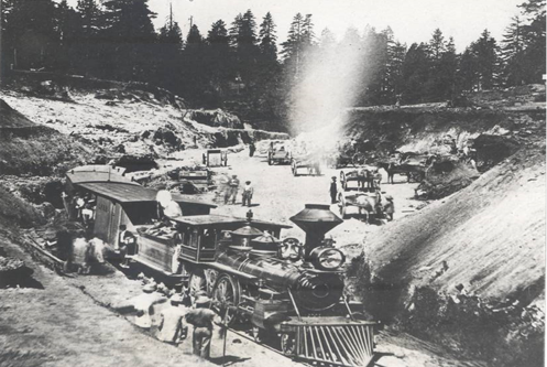 Monochrome image with large locomotive in foreground, workers in background