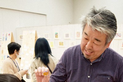 障害のある人たちがデザインした線画に色を塗って缶バッジを作るイベントで、来場の子どもたちと交流する樋口龍二さん（右）＝福岡県筑後市で2025年2月1日、青木絵美撮影