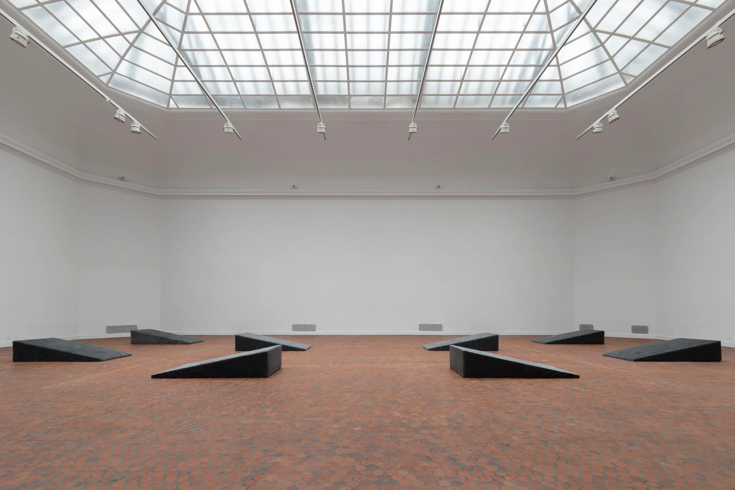 A skylit gallery with eight grey wedges placed across the floor.