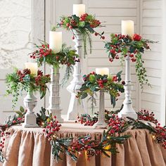 christmas decorations are displayed on a table in front of a window with candles and greenery