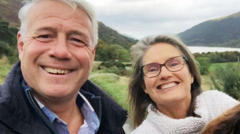 A selfie of Scott and Jenny Hastings standing outdoors with a valley in the backdrop