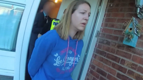 Lucy Letby, wearing a blue hooded top, is led from the front door of her home.