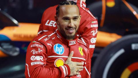 Lewis Hamilton holds his right hand across his chest while wearing the Ferrari race uniform