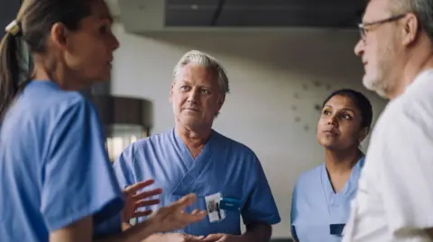 Two men and two women standing in a circle wearing medical scrubs. Stock Image